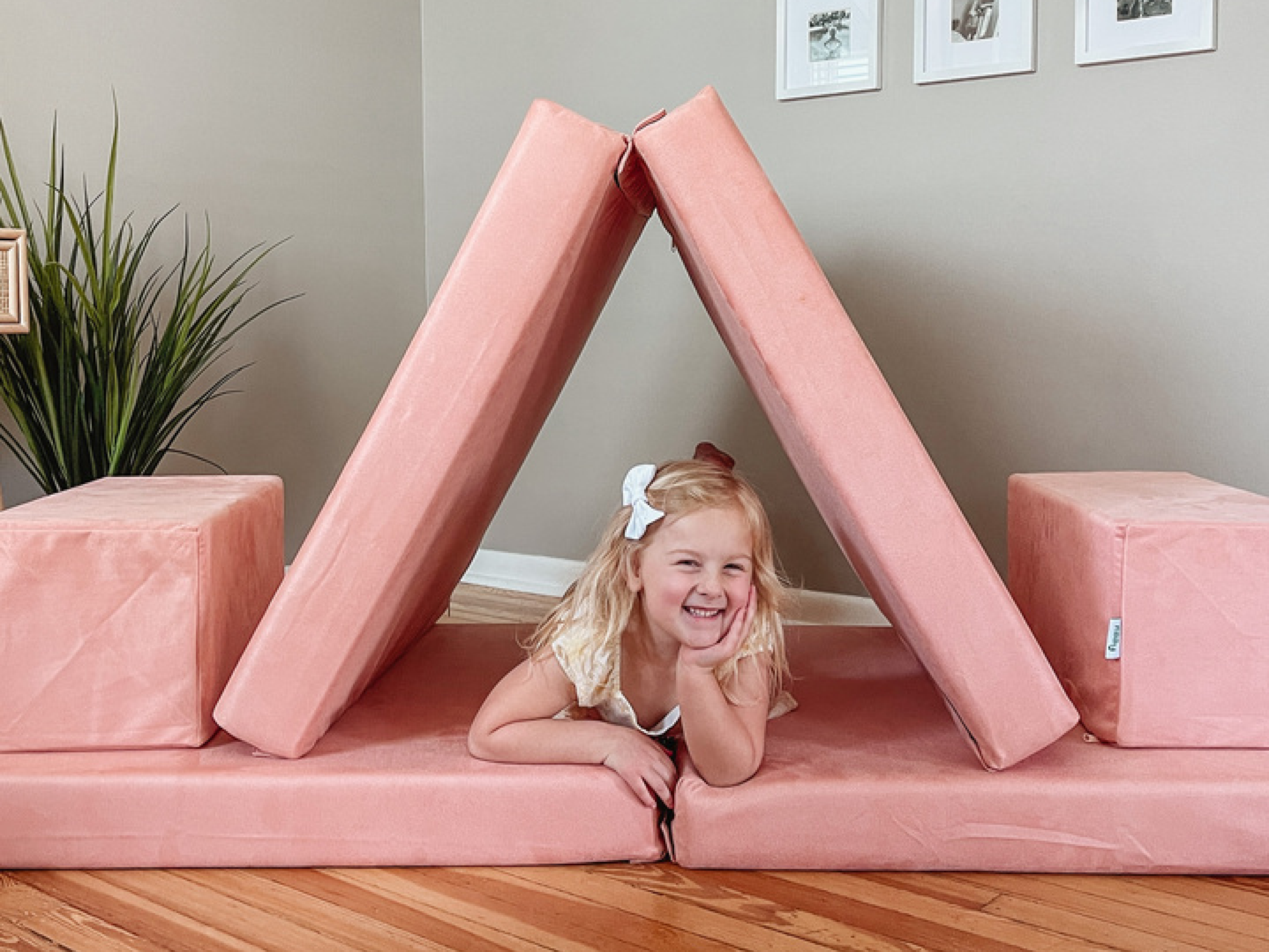 Child playing on a pink foam play set in a room with a plant and framed pictures.